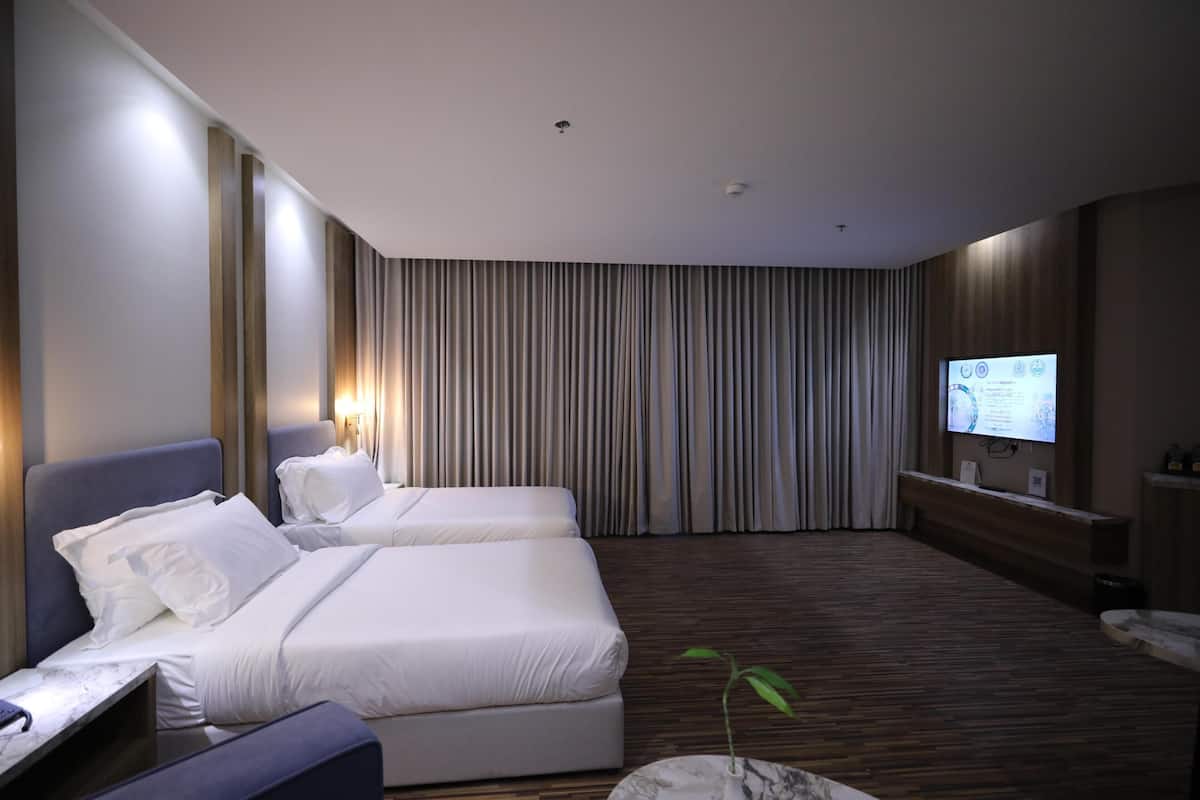 A hotel room with two beds, a TV, a plant, and a wooden floor.