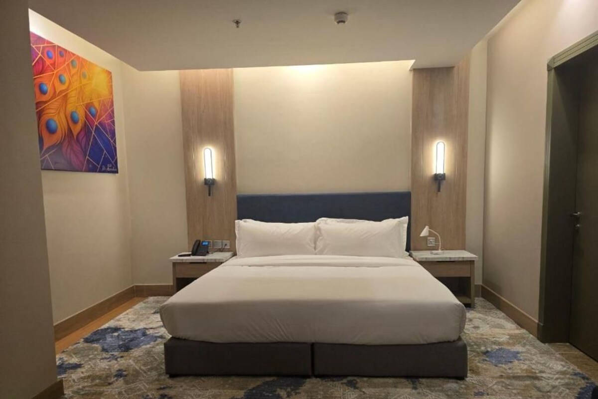 Una habitación de hotel con una cama grande, dos mesitas de noche, una obra de arte en la pared y una puerta.