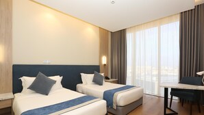 A hotel room with two beds, a dining table, and a view of the city.