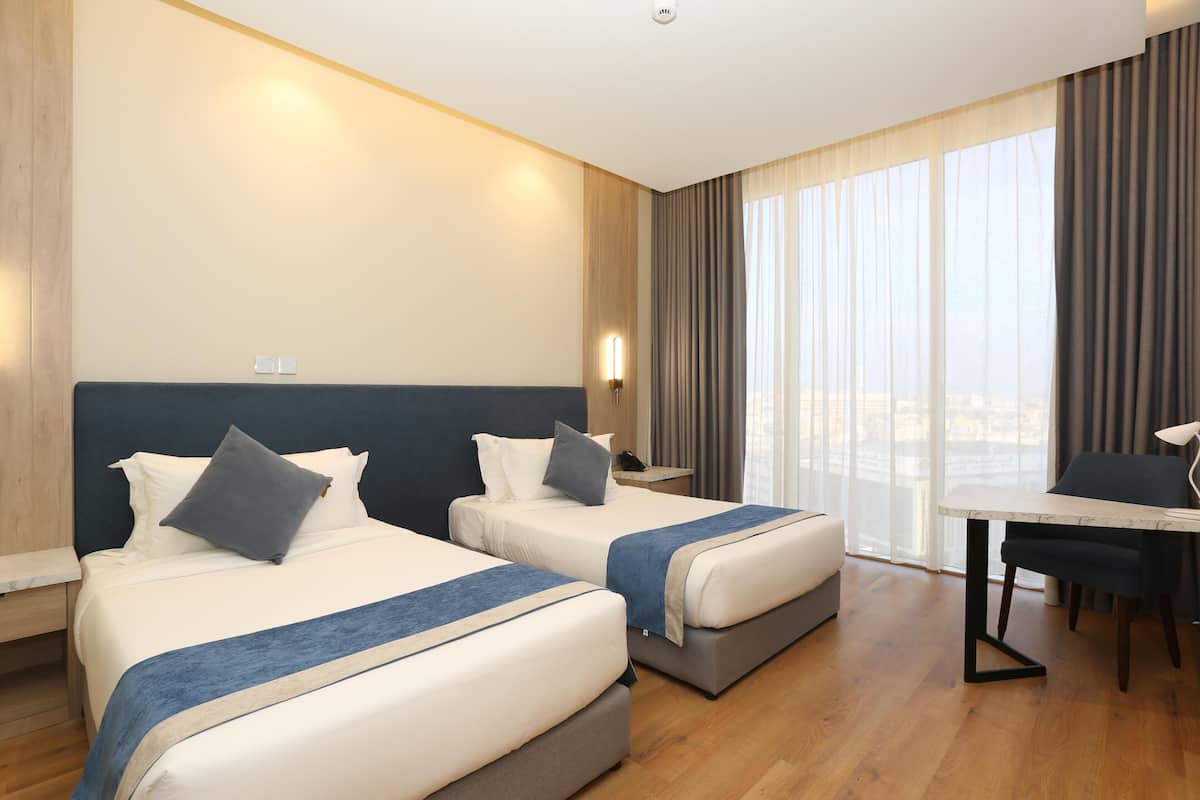 A hotel room with two beds, a dining table, and a view of the city.