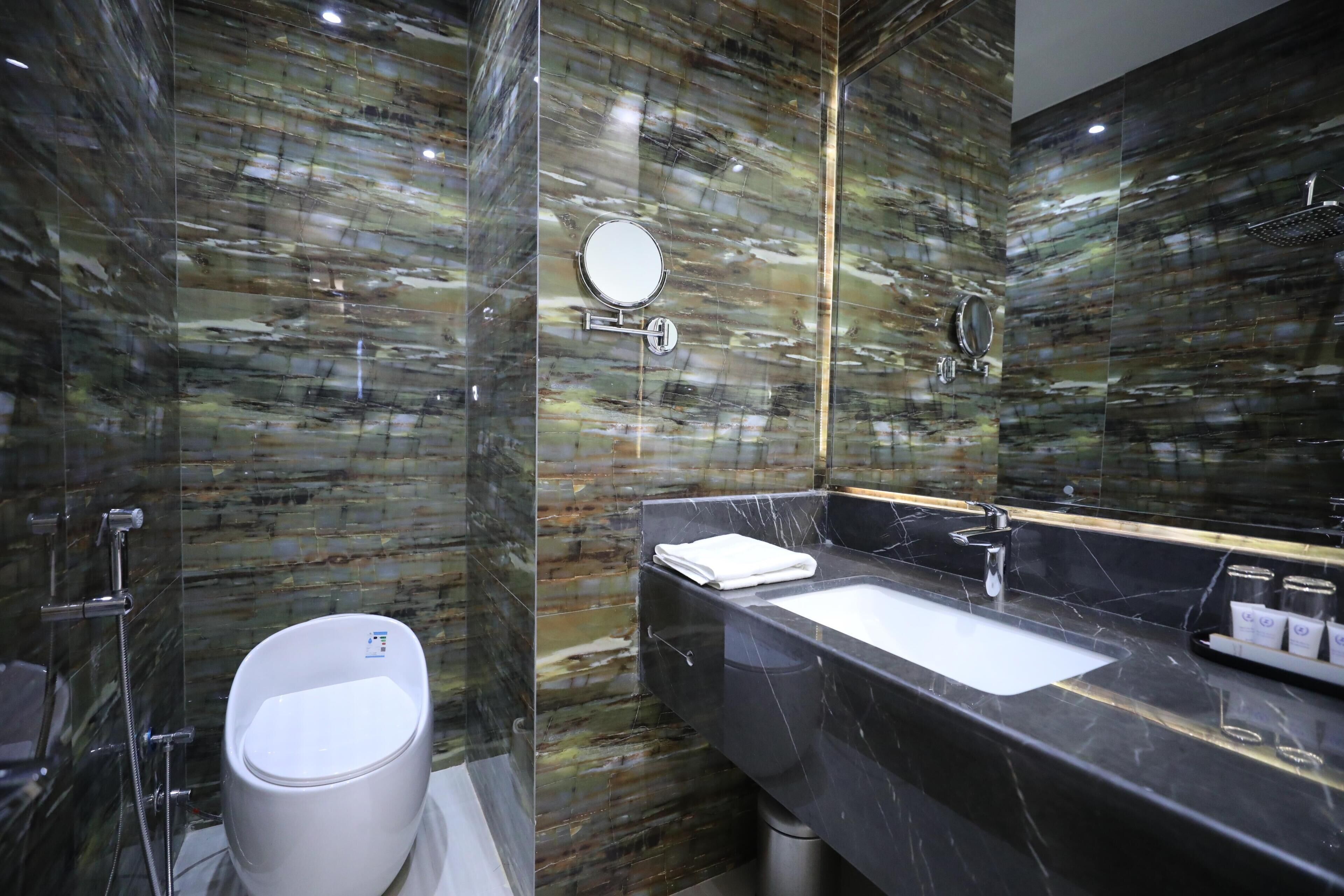 A modern bathroom with a marble wall, a white toilet, a sink with a mirror, and a shower area.