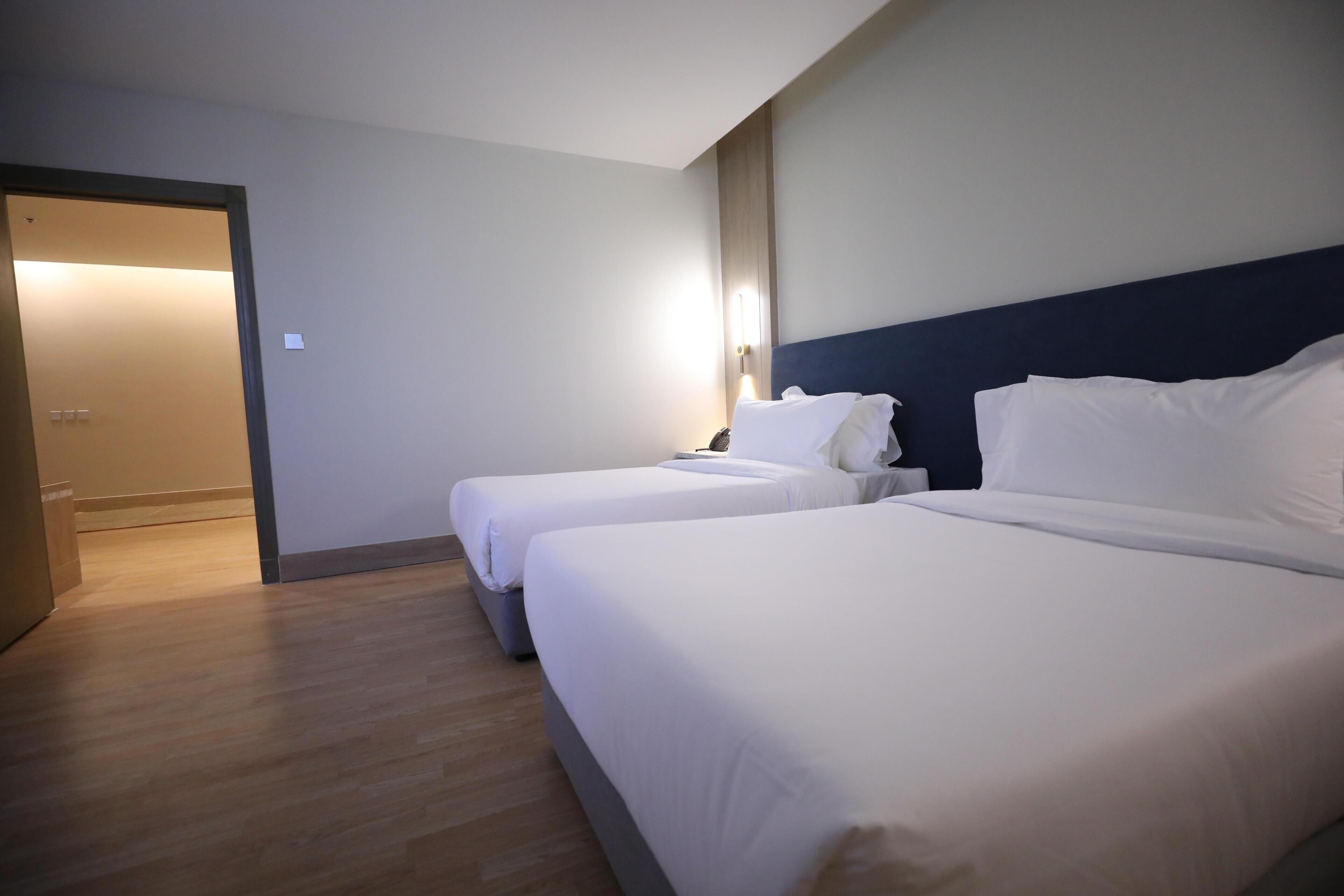 Une chambre d’hôtel avec deux lits, un plancher en bois, une porte et un luminaire fixé au mur.