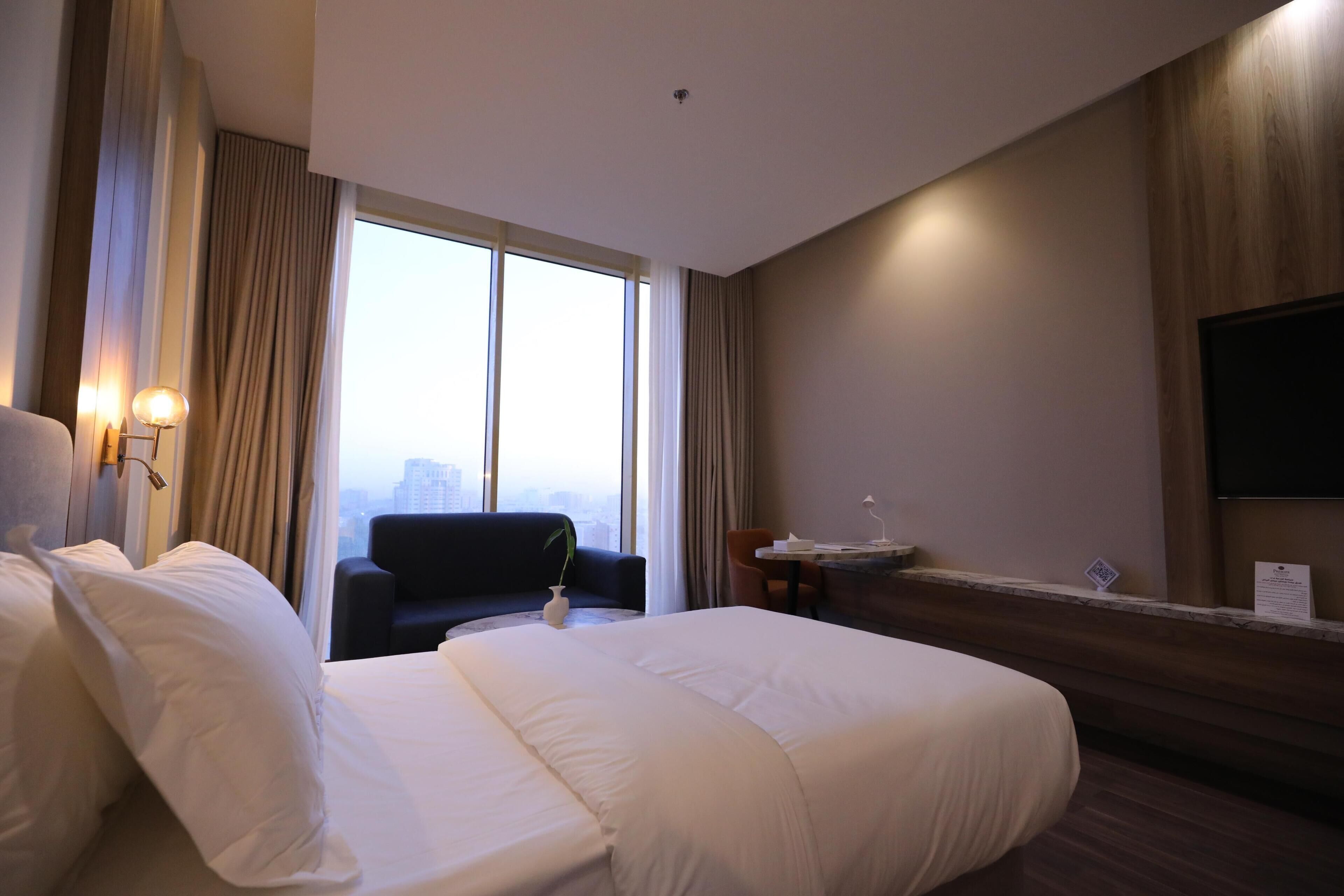 A hotel room with two beds, a desk, a chair, a TV, and a large window with curtains.