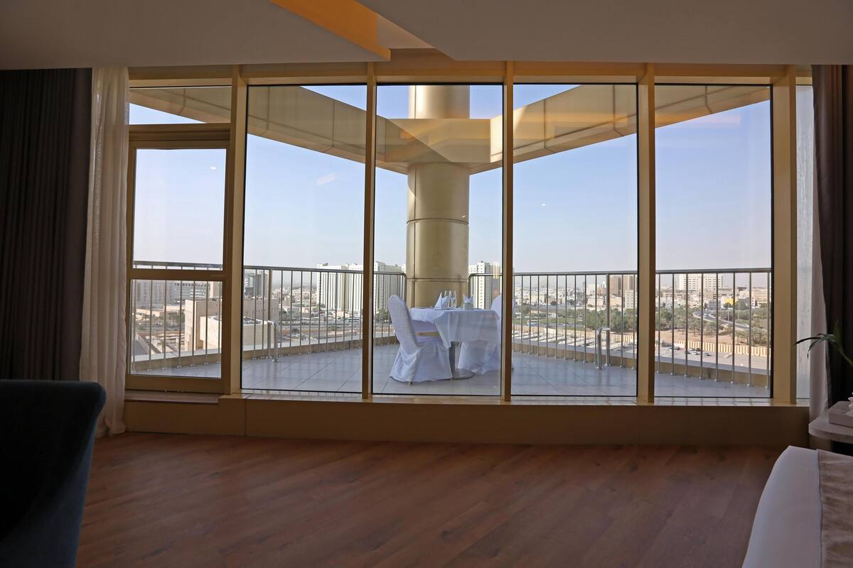 A room with a large window, a balcony with a table and chairs, and a bed.