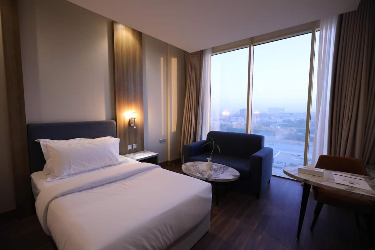 A hotel room with a bed, a sofa, a small table, and a view of the city.