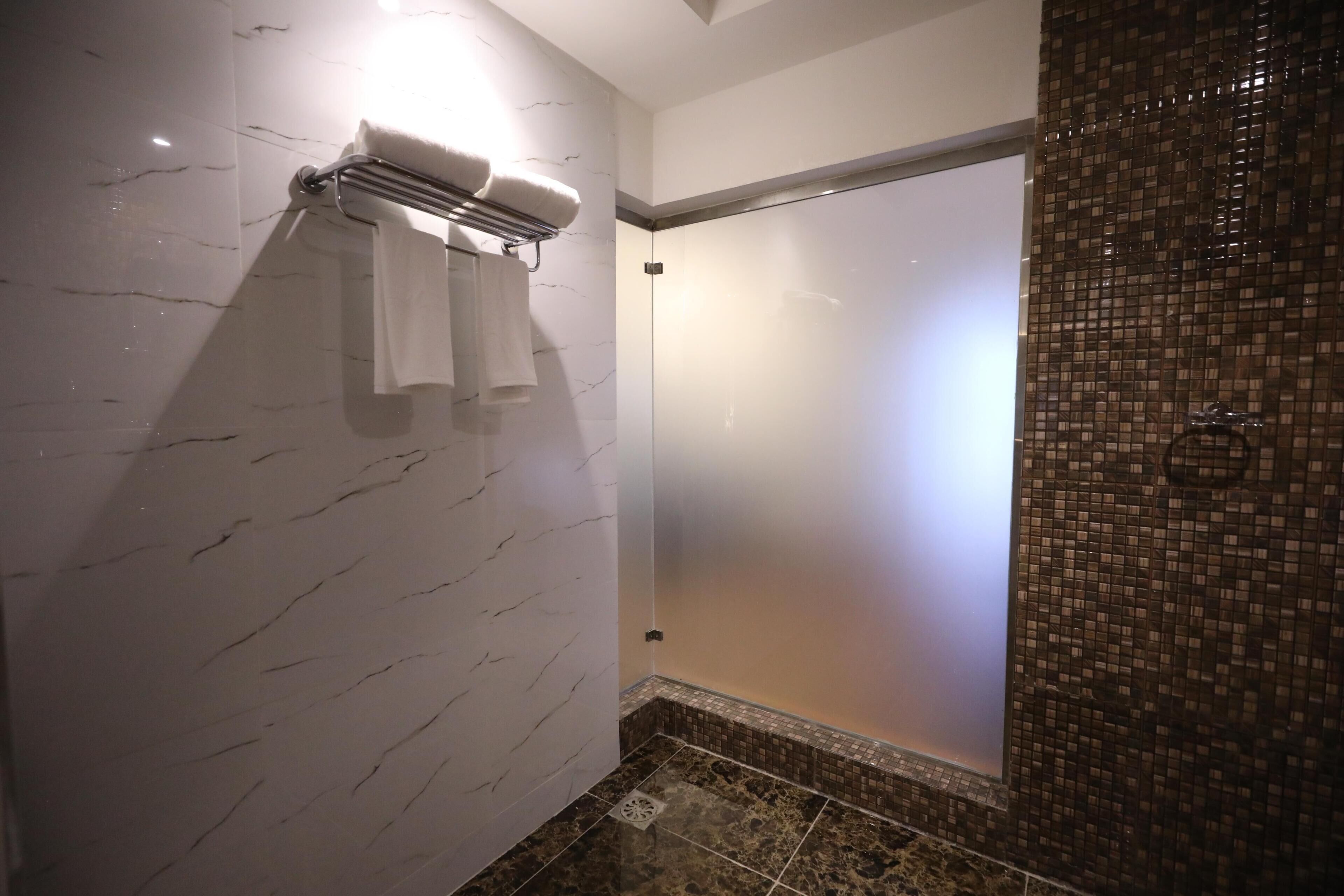 A modern bathroom with a glass shower enclosure, a towel rack, and a marble wall.