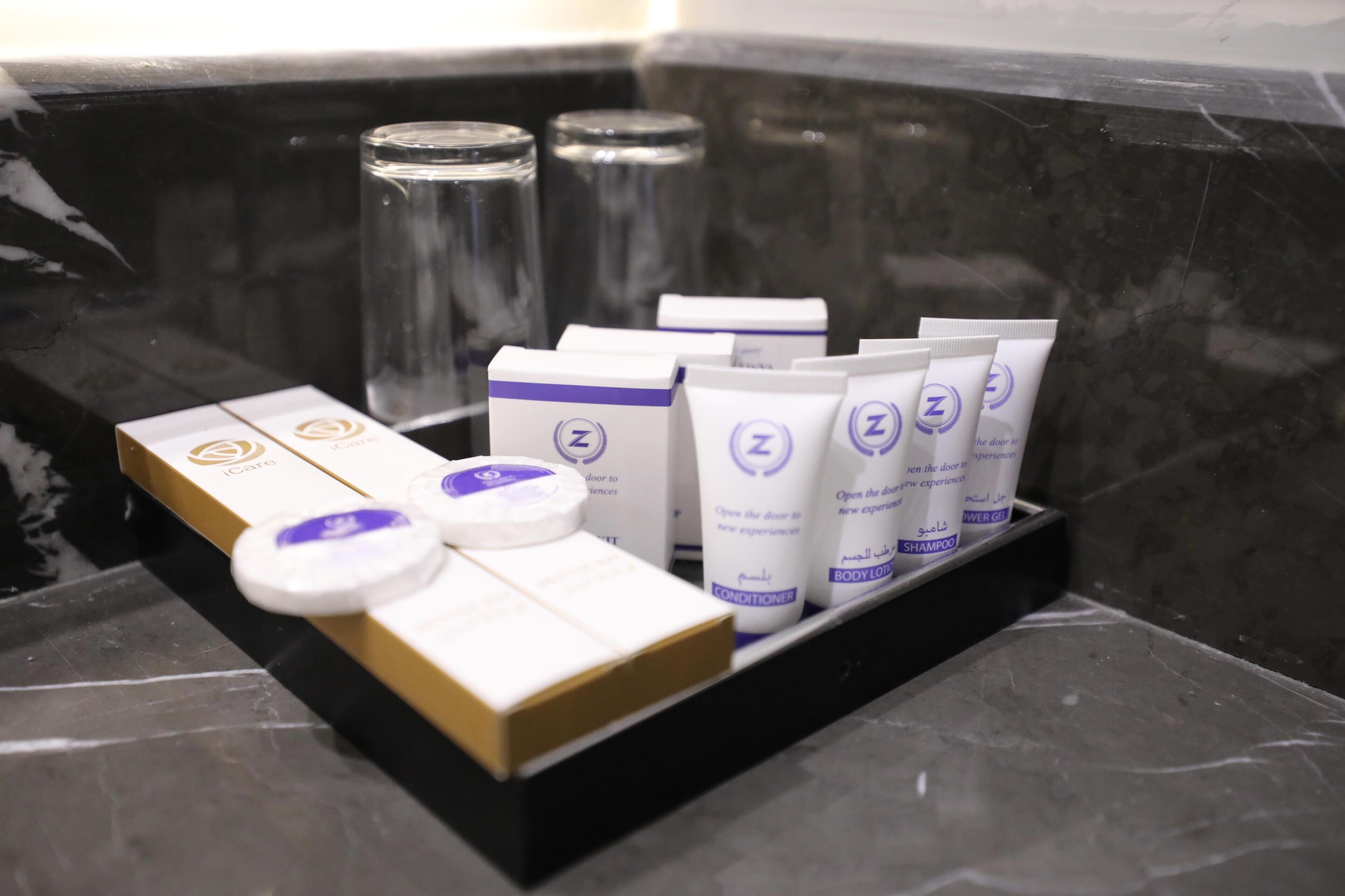 A bathroom with a black marble sink, a glass container, and a tray holding toiletries including a conditioner, body lotion, and shampoo.
