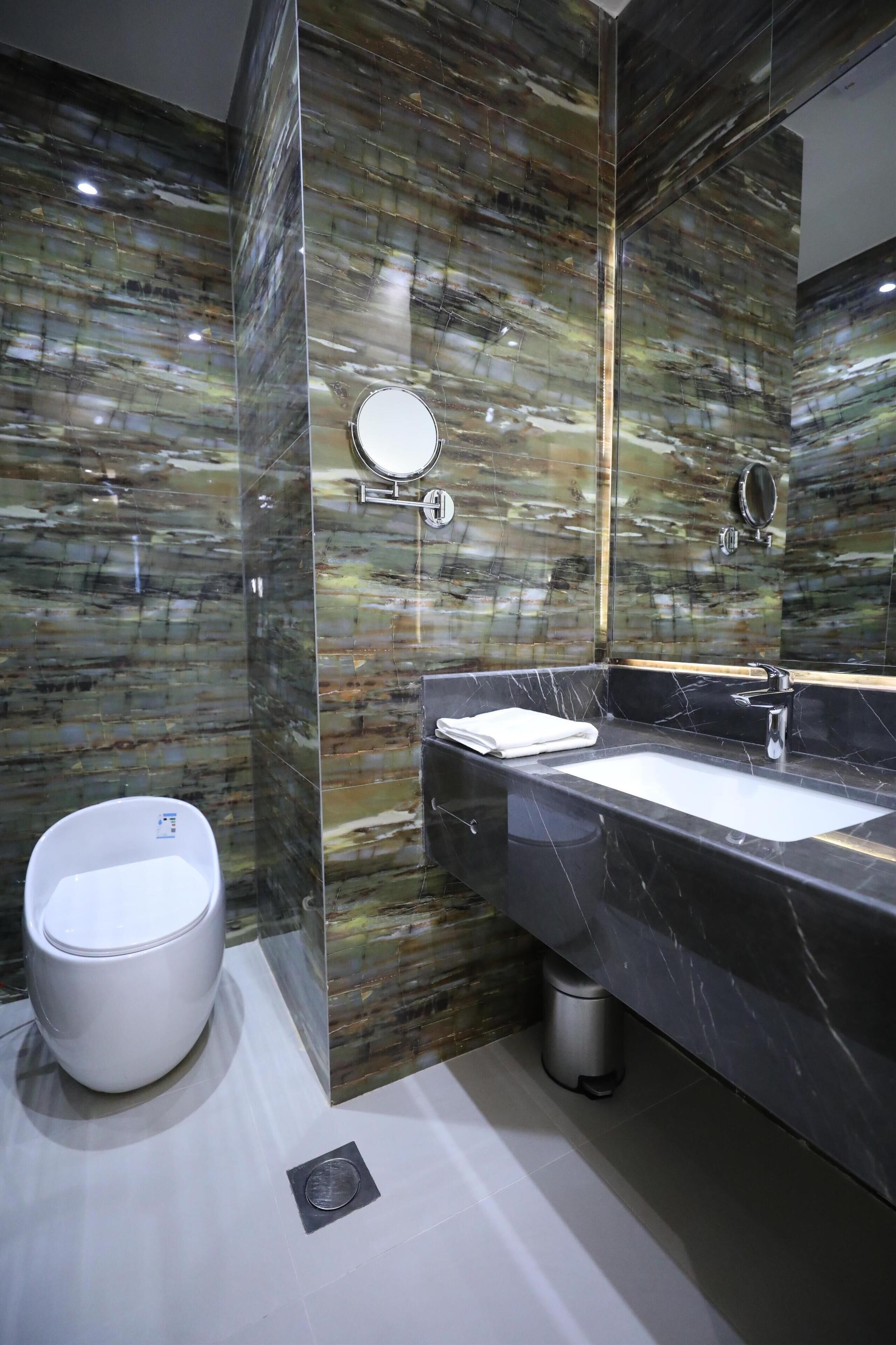 A modern bathroom with a marble vanity, a toilet, and a mirror.