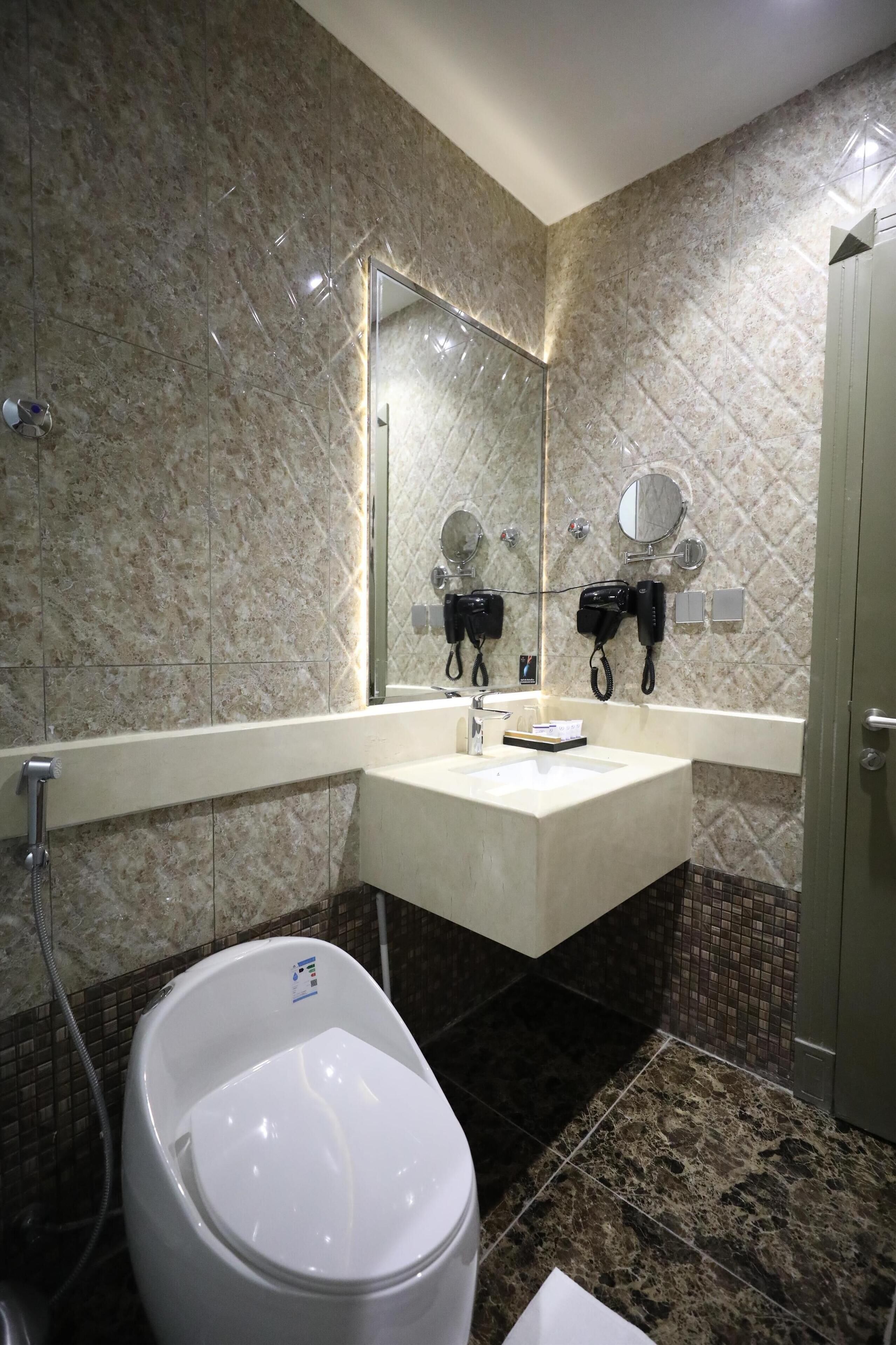 A bathroom with a marble wall, a sink, a mirror, a toilet, and a shower area.