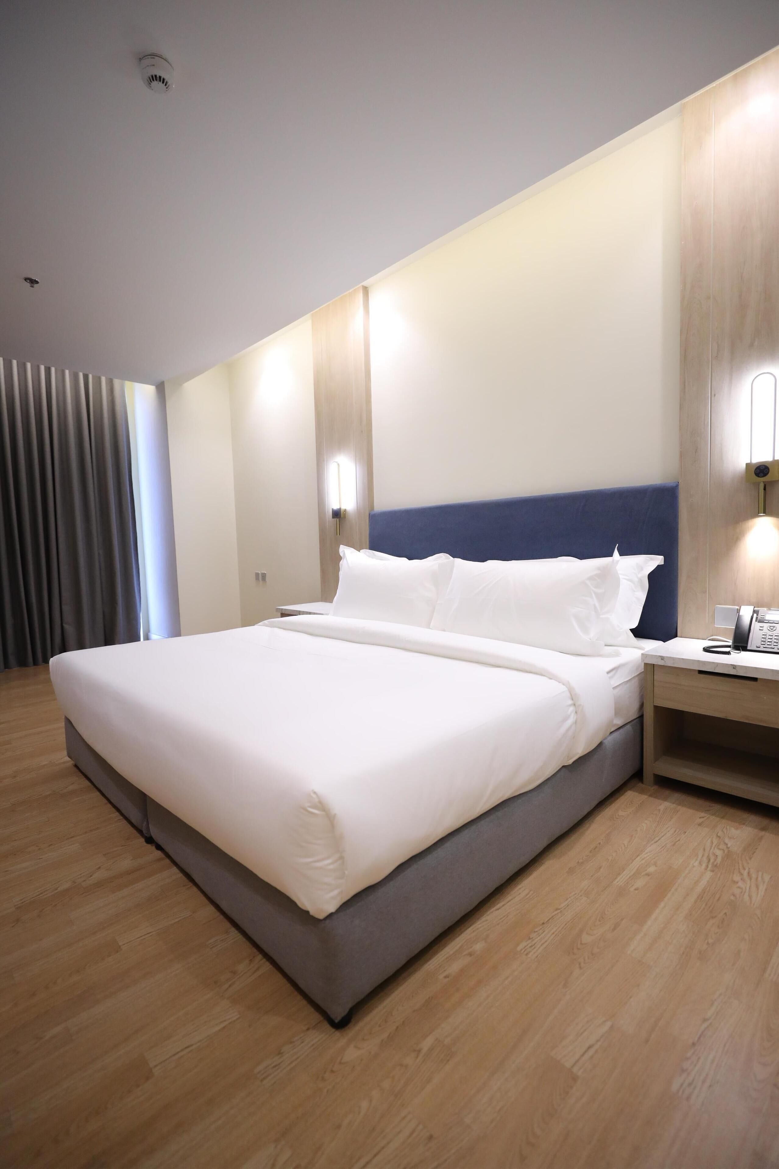 A hotel room with a large bed, a bedside table with a phone, and a wall-mounted light.