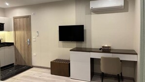 A compact hotel room with a kitchenette, a flat-screen TV mounted on the wall, a desk with a chair, and a small trash bin. - Deluxe Room at Stay Inn 51 Hotel (2 Adults + 1 Child) (Banī Ghālib)