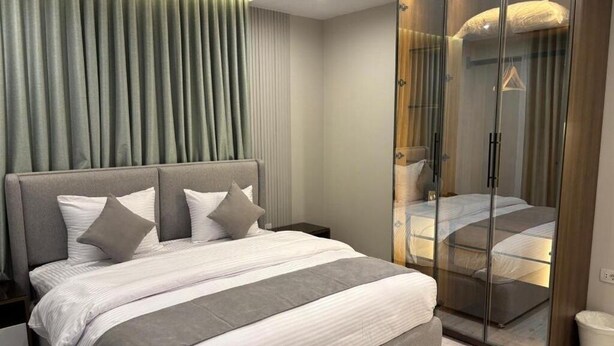 A modern bedroom with a large bed, a glass wardrobe, and a headboard with vertical lines. - Deluxe Room at Stay Inn 51 Hotel (2 Adults + 1 Child) (Banī Ghālib)