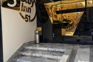 A hotel entrance with a marble staircase, a trash bin, and a reflective glass wall with a geometric design. - Deluxe Room at Stay Inn 51 Hotel (2 Adults + 1 Child) (Banī Ghālib)