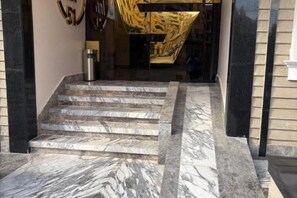 A set of marble steps leading to a building entrance with a glass door and a golden abstract sculpture above it. - Stay Inn 51 Hotel – Cozy Family Rooms for Your Perfect Getaway (Banī Ghālib)