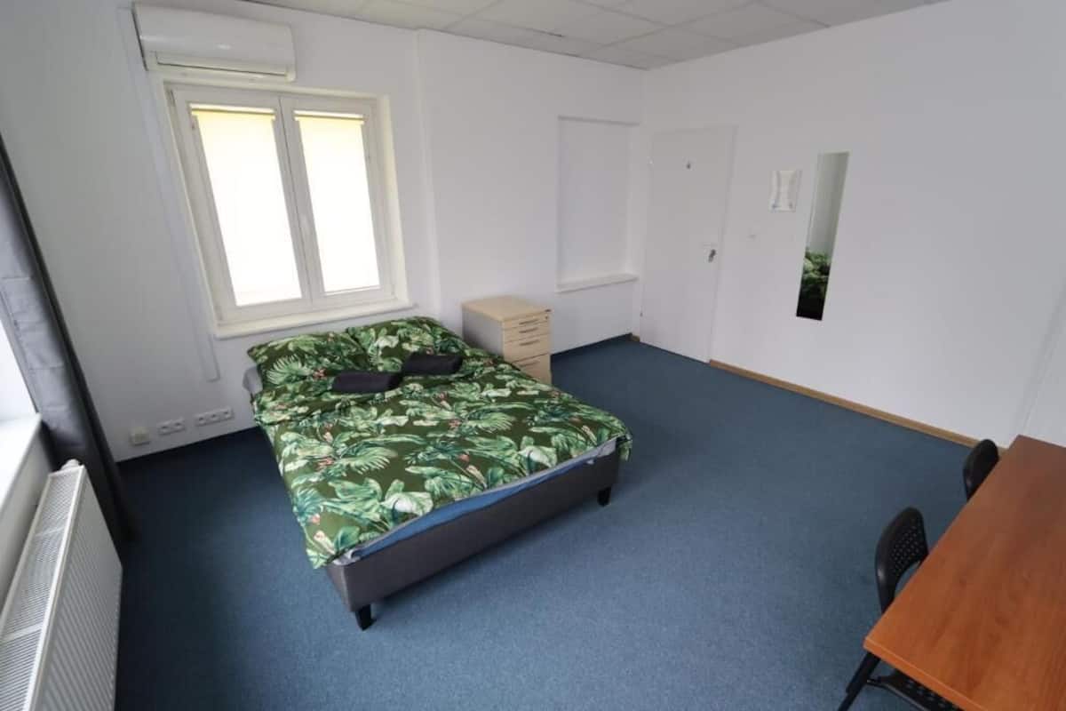 A room with a bed, a desk, a chair, a radiator, a window, and a door.