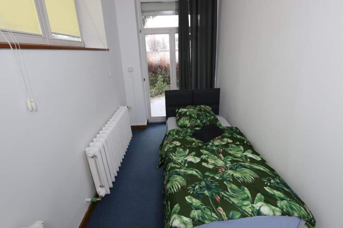 A small bedroom with a single bed, a radiator, and a view of the outdoors through a door.