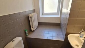 A small bathroom with a toilet, a sink, a window, and a radiator. - Fantastic Inn Warsaw - FMG (Warsaw)