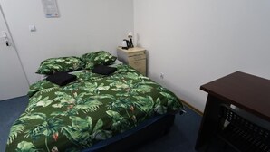 A single bed with a green leaf-patterned bedspread, a small wooden nightstand with a lamp, and a desk with a chair. - Fantastic Inn Warsaw - FMG (Warsaw)