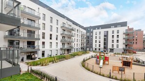 A modern apartment building with multiple balconies, a playground, and a landscaped courtyard. - Modern Studio in Wrzeszcz | Balcony | Close to the Station (Gdańsk)