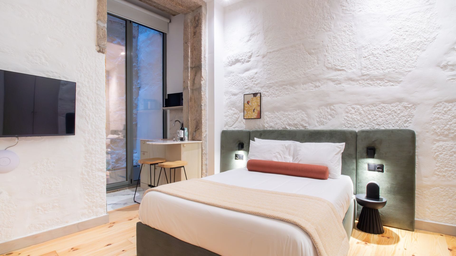 Ein modernes Schlafzimmer mit einem großen Bett, einem an der Wand befestigten Fernseher und einer kleinen Küchenzeile.