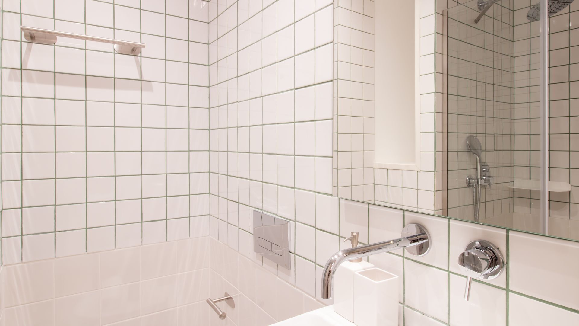 A modern bathroom with white subway tiles, a glass shower enclosure, a handheld showerhead, and a chrome sink.