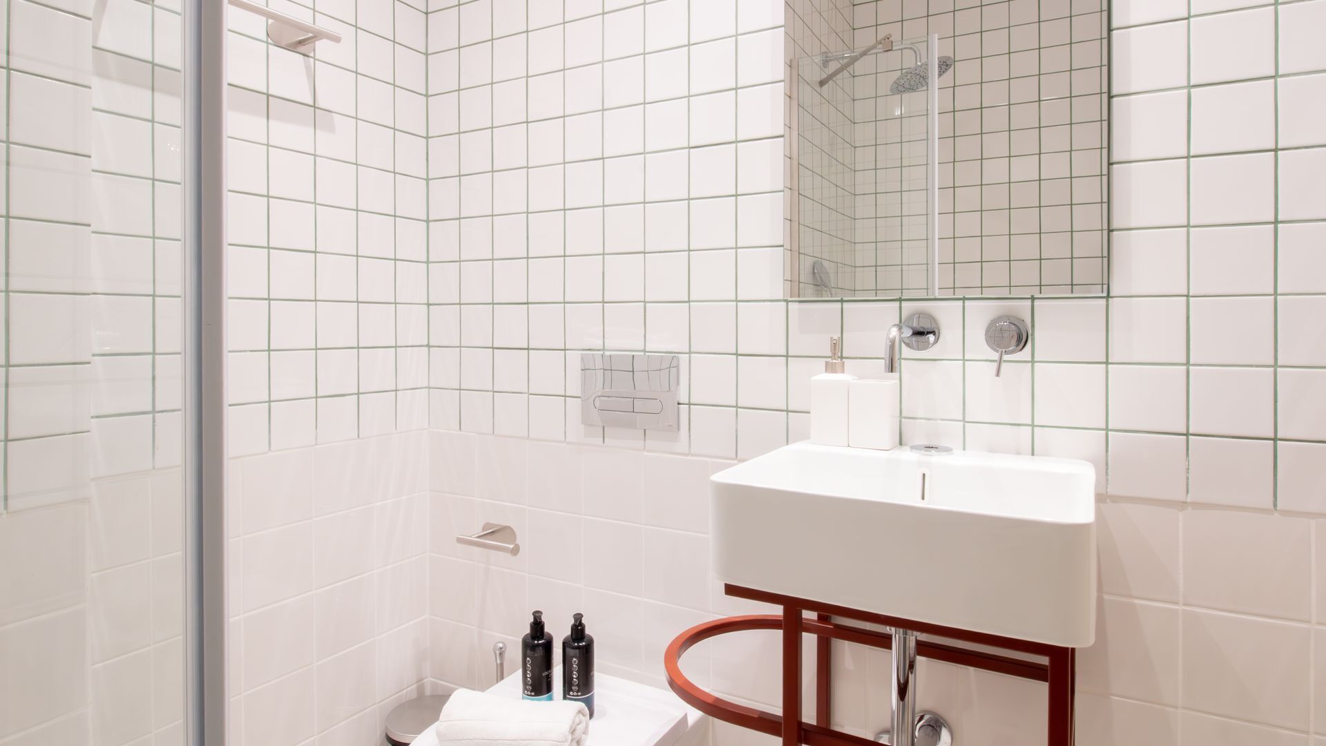 A modern bathroom with white tiles, a glass shower enclosure, a white sink with chrome fixtures, and a mirror above the sink.
