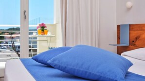Camera d'albergo con un letto, una testiera in legno, una finestra con tende e un balcone con tavolo e fiori.