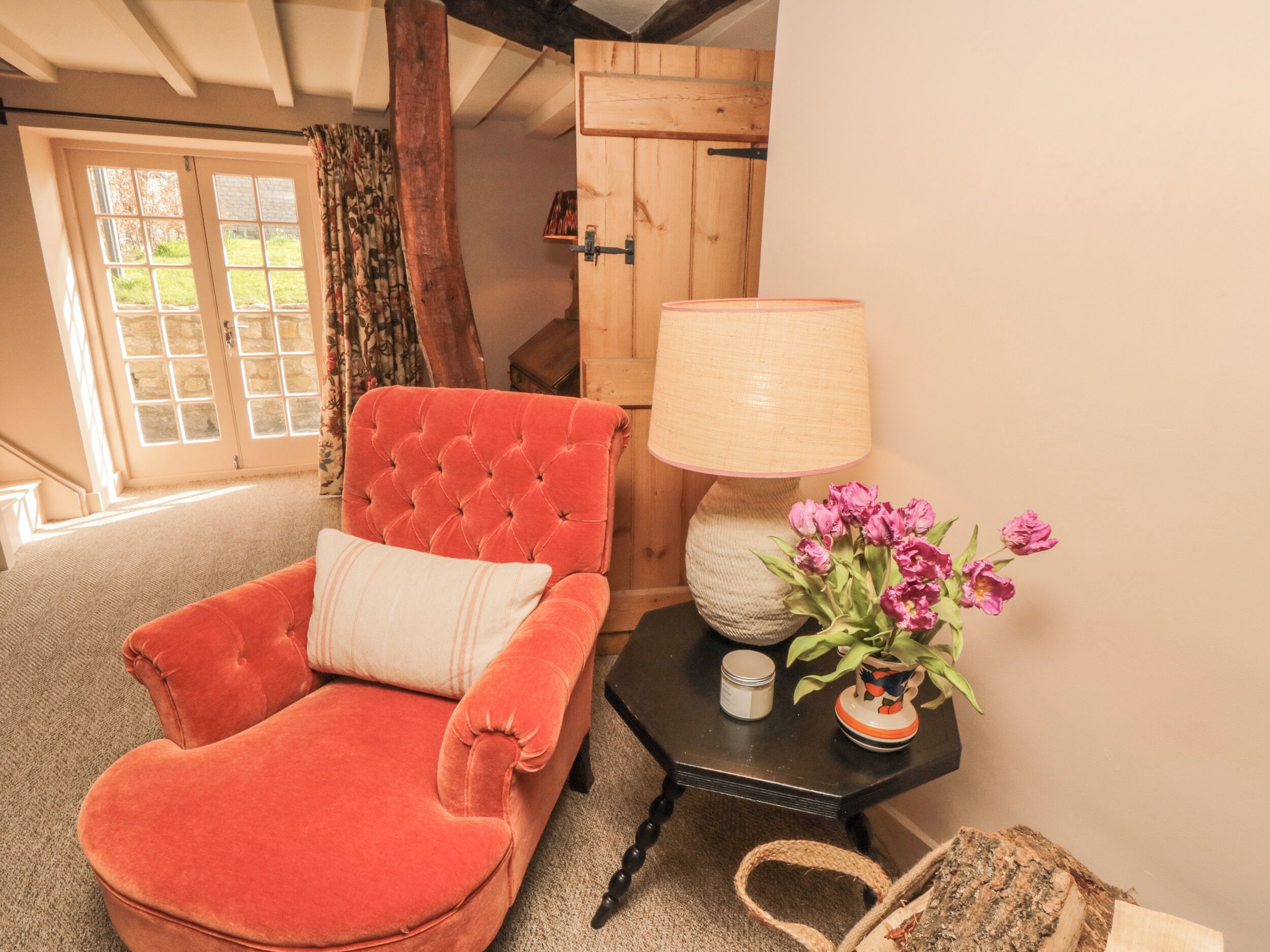 A cozy room with a red velvet armchair, a wooden door, a lamp, and a vase of flowers.