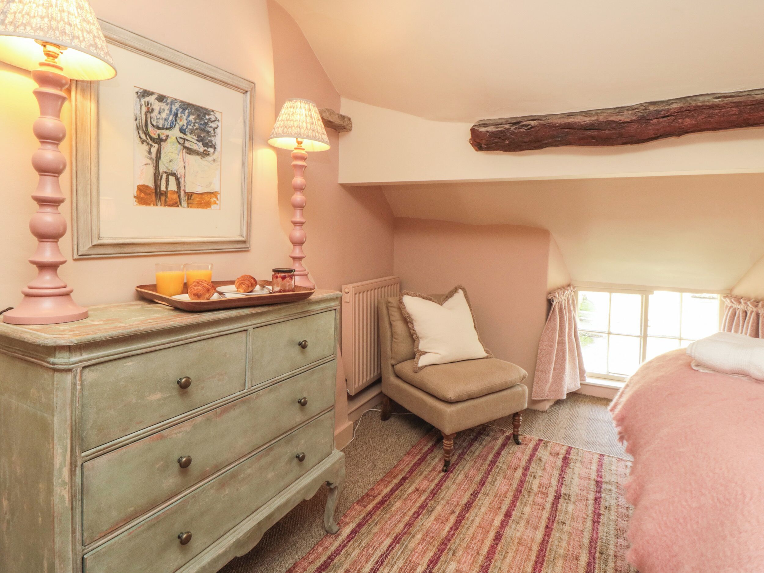 A cozy bedroom with a dresser, a chair, a bed, and a window with curtains.