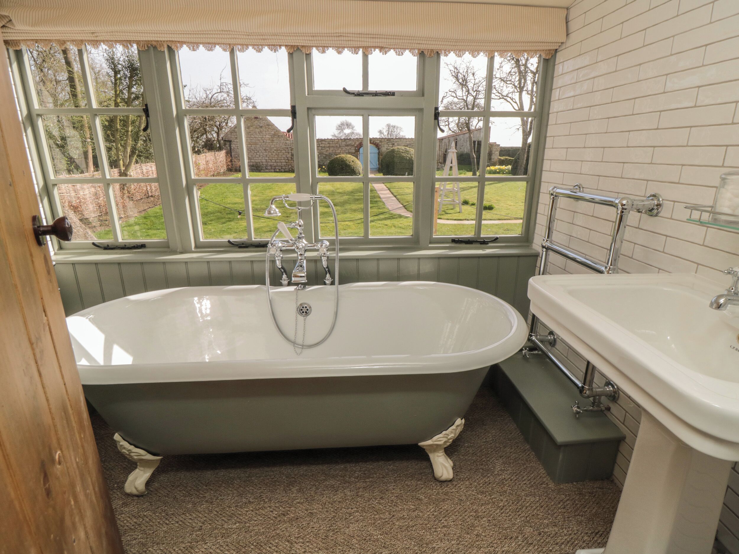 A bathroom with a freestanding bathtub, a sink, and a window with a view of a garden.