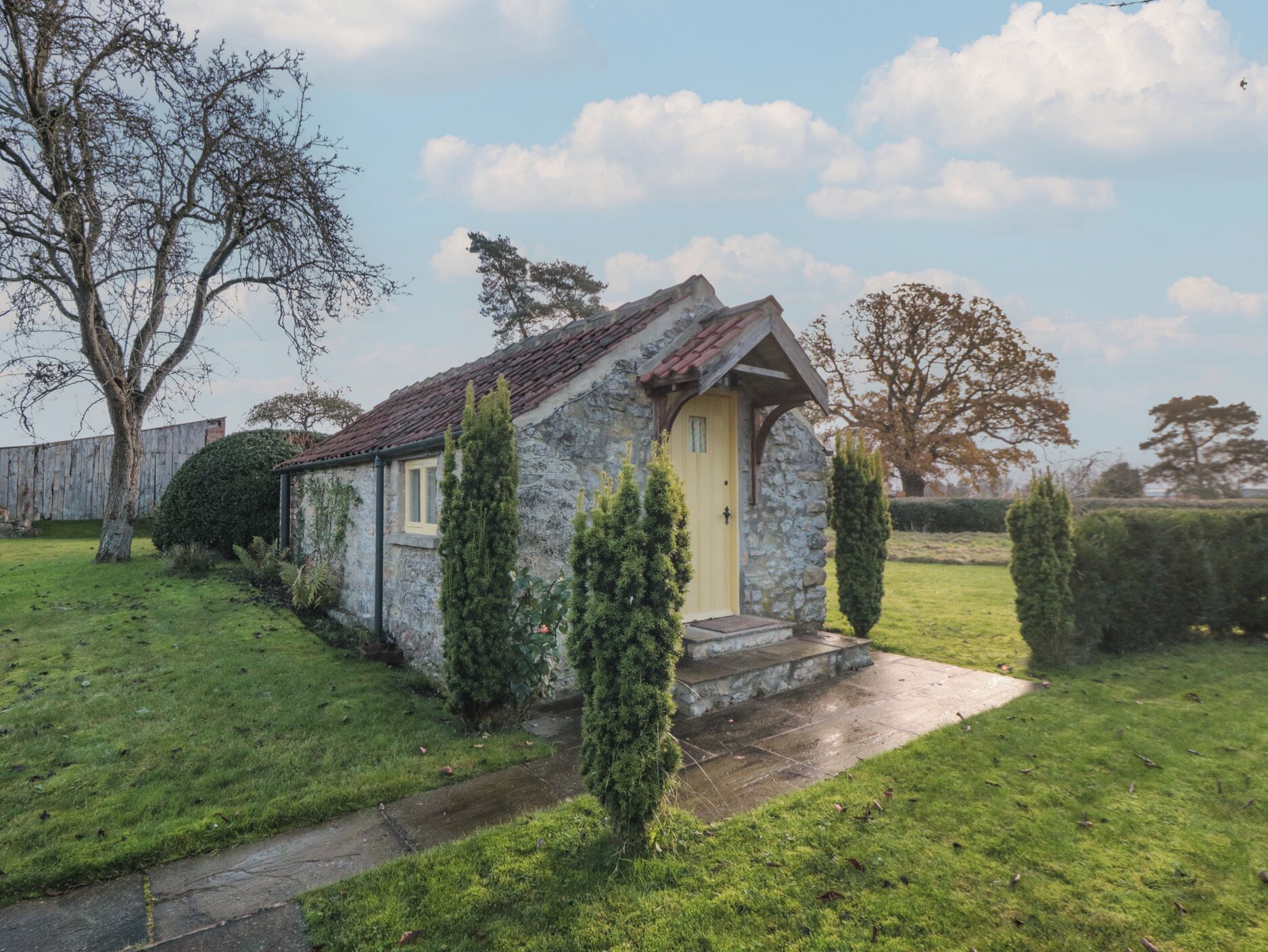 A small stone house with a yellow door, surrounded by a well-maintained lawn and a few trees.