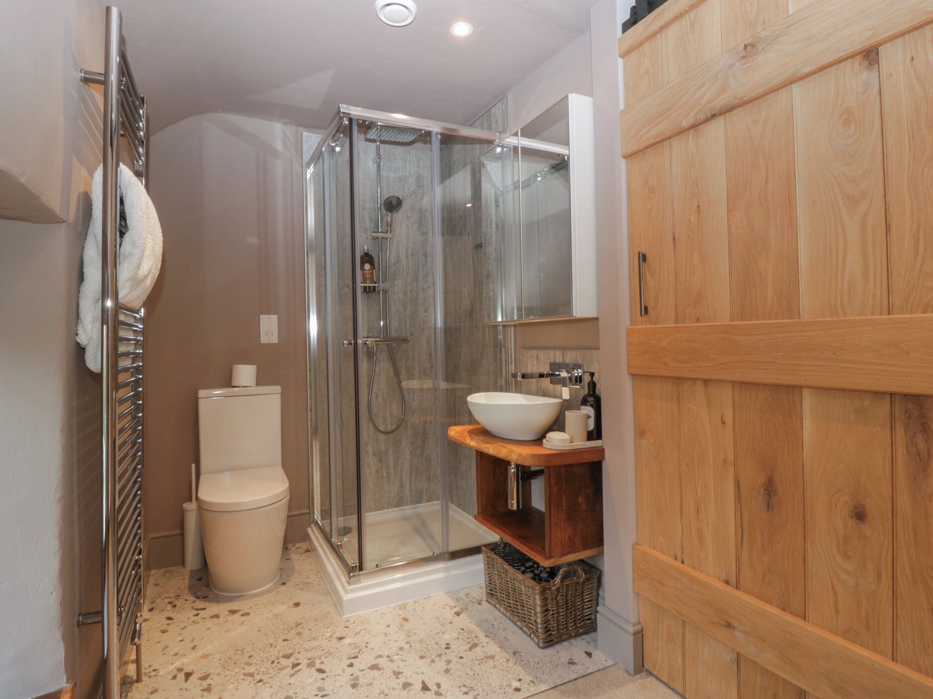 Un baño moderno con ducha de vidrio, inodoro y tocador de madera con lavamanos.