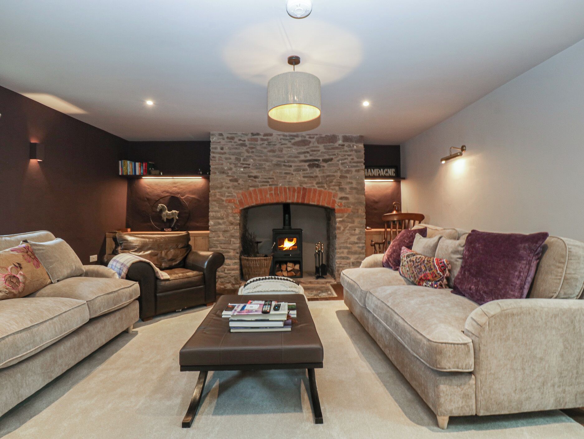 A cozy living room with a stone fireplace, two sofas, a coffee table with books, and a chandelier.