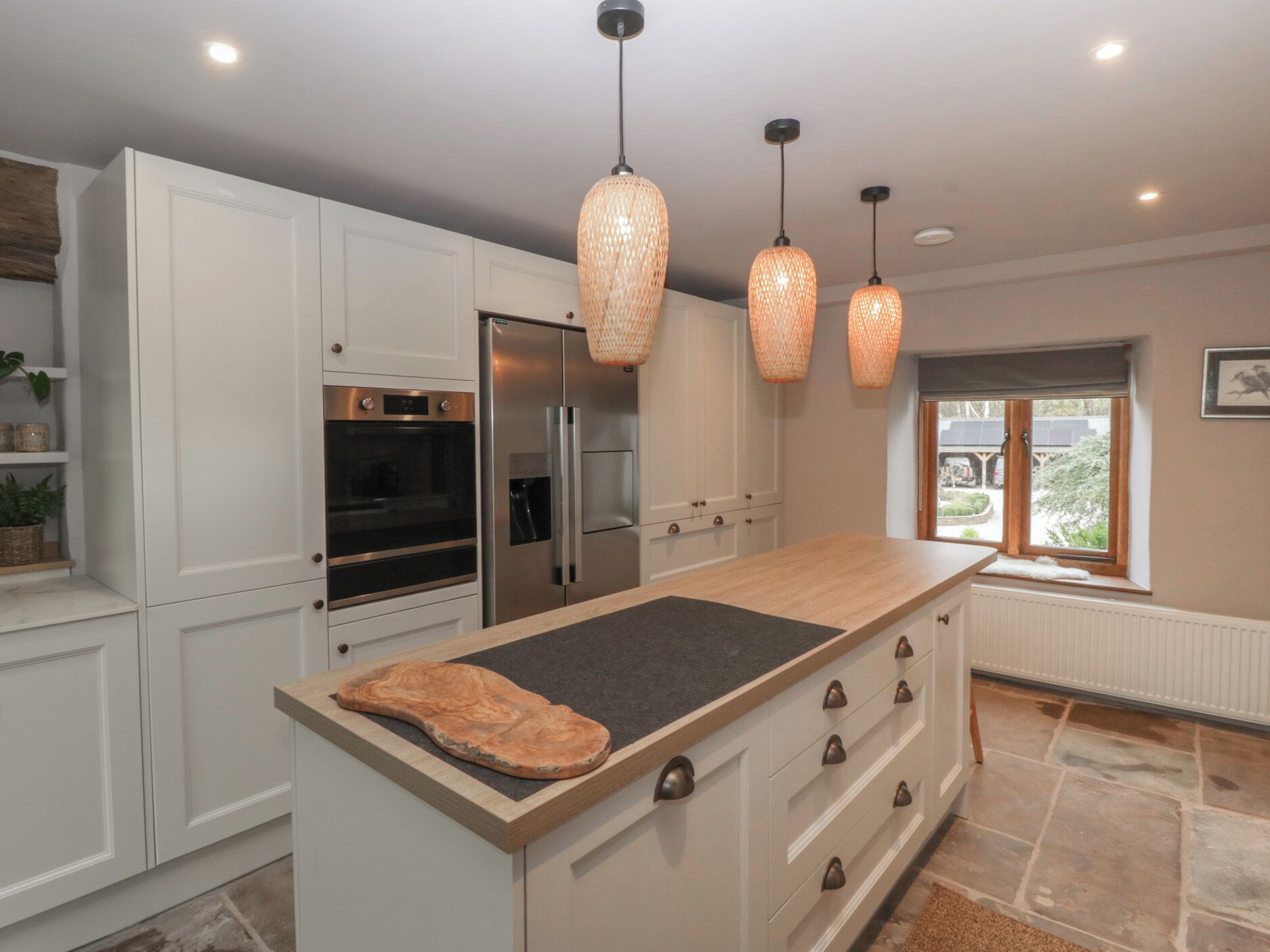 Una cocina moderna con armarios blancos, una isla grande, electrodomésticos de acero inoxidable e iluminación colgante.