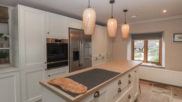 Una cocina moderna con armarios blancos, una isla grande, electrodomésticos de acero inoxidable e iluminación colgante.