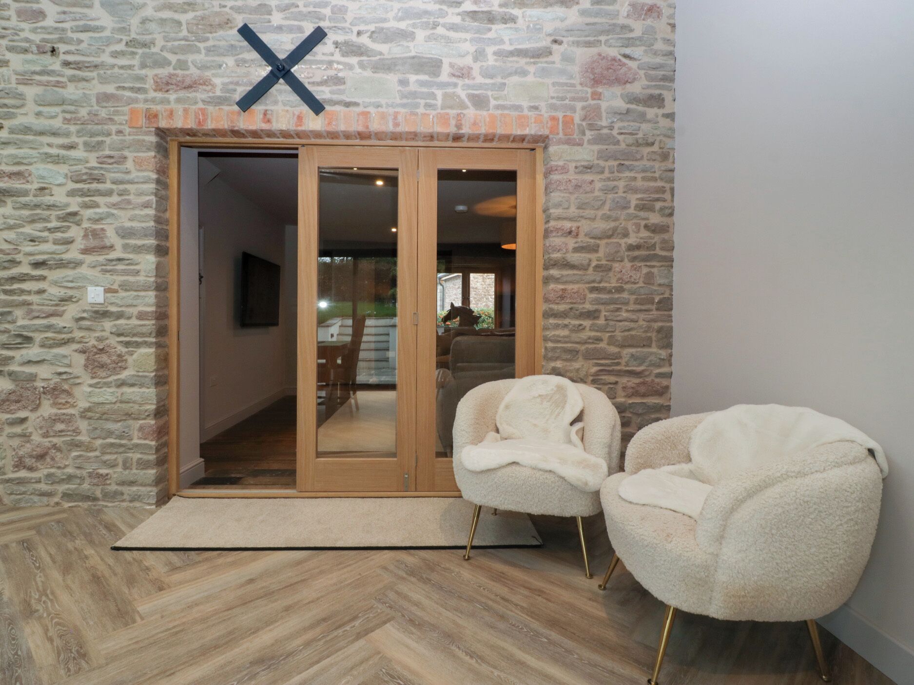 A room with a stone wall, a wooden door, two plush chairs, and a herringbone-patterned floor.