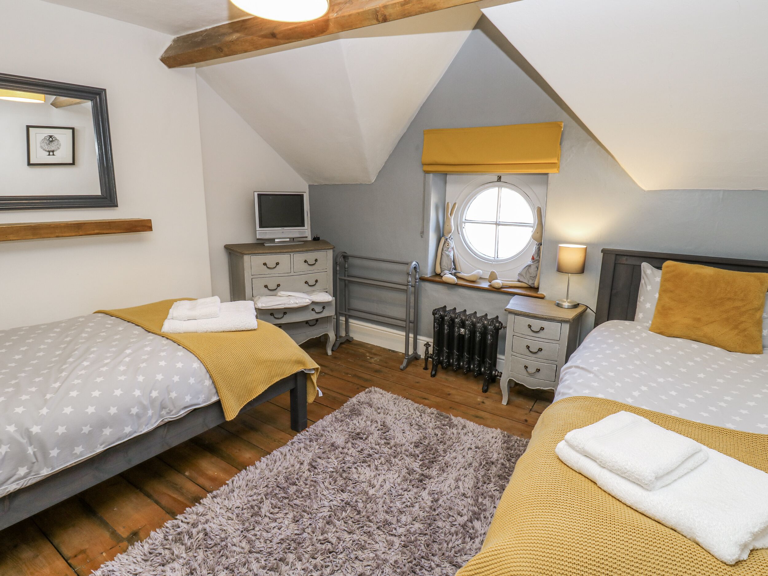 A bedroom with two beds, a television, a radiator, and a window with a view.