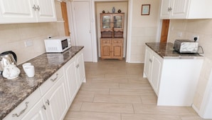 A kitchen with white cabinetry, granite countertops, a microwave, a toaster, and a cabinet with glass doors. - Cherry Trees (Haverfordwest)