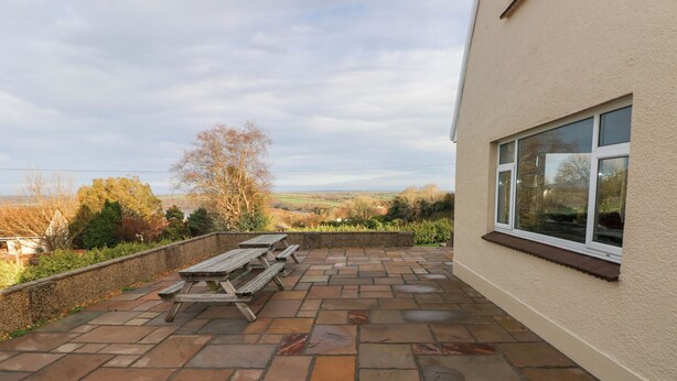 A patio with stone flooring and picnic tables, overlooking a scenic landscape. - Cherry Trees (Haverfordwest)