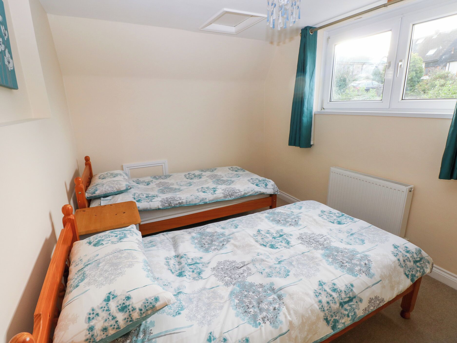 A bedroom with two single beds, a window with curtains, and a radiator.
