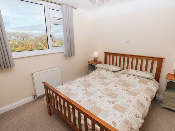 Une chambre à coucher avec un lit en bois, une fenêtre avec des rideaux, une table de chevet avec une lampe et un radiateur.