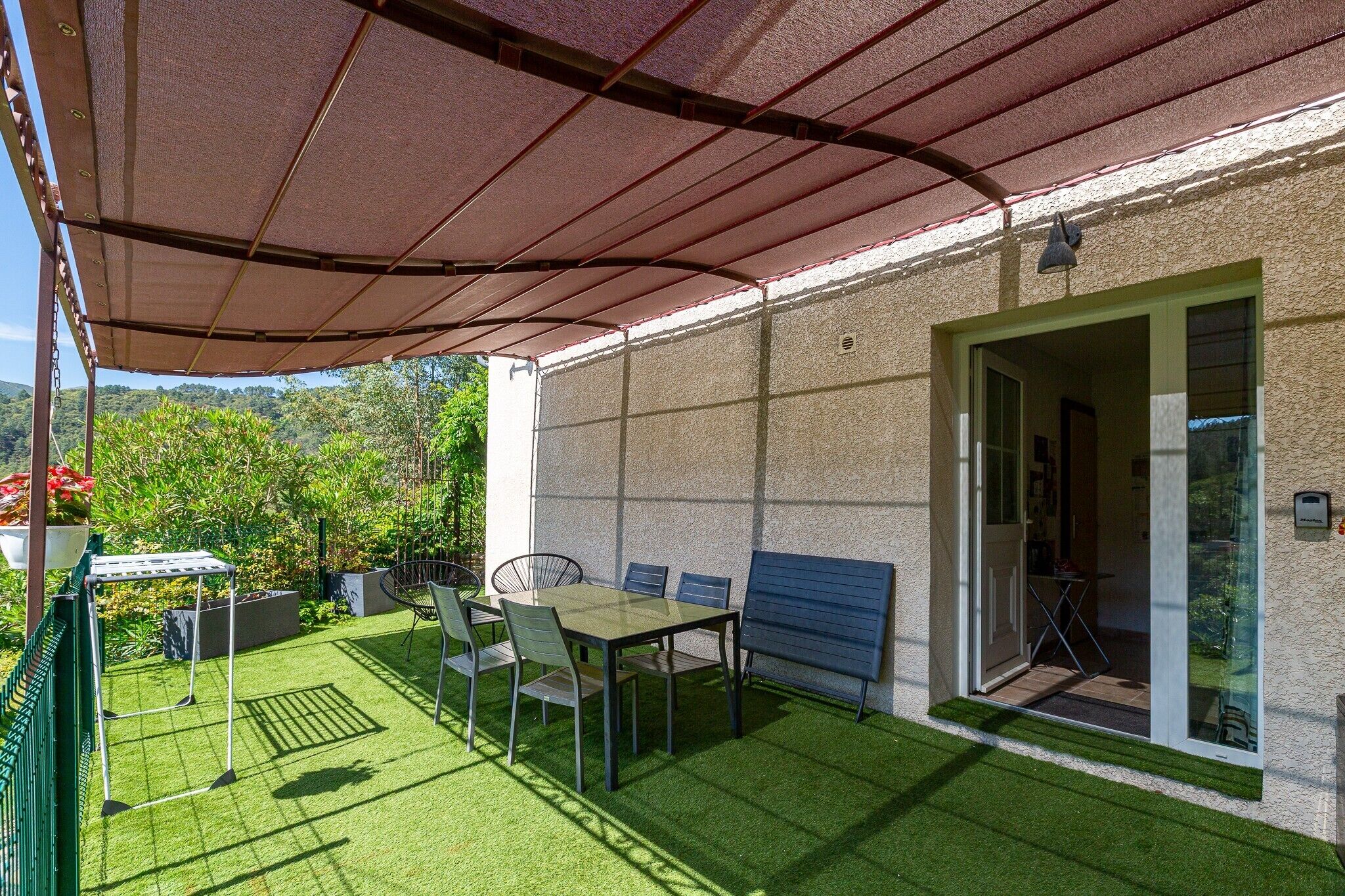 A covered patio with a table and chairs, a hanging chair, and a view of the surrounding greenery.
