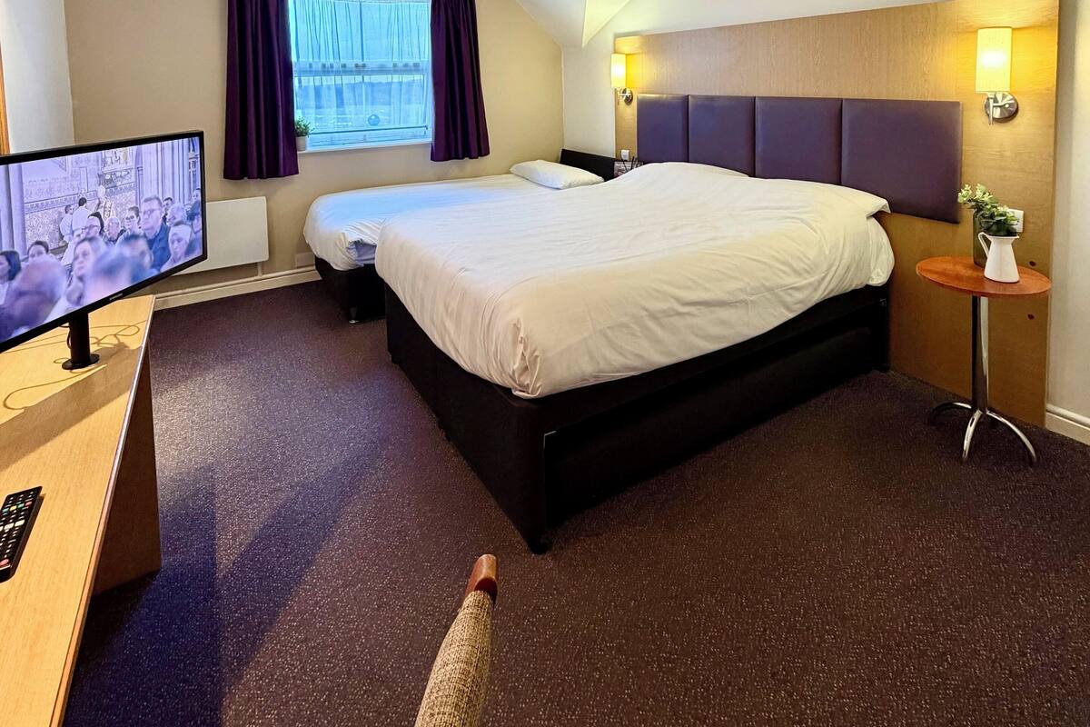 Una habitación de hotel con una cama grande, un televisor sobre un escritorio y una ventana con cortinas.