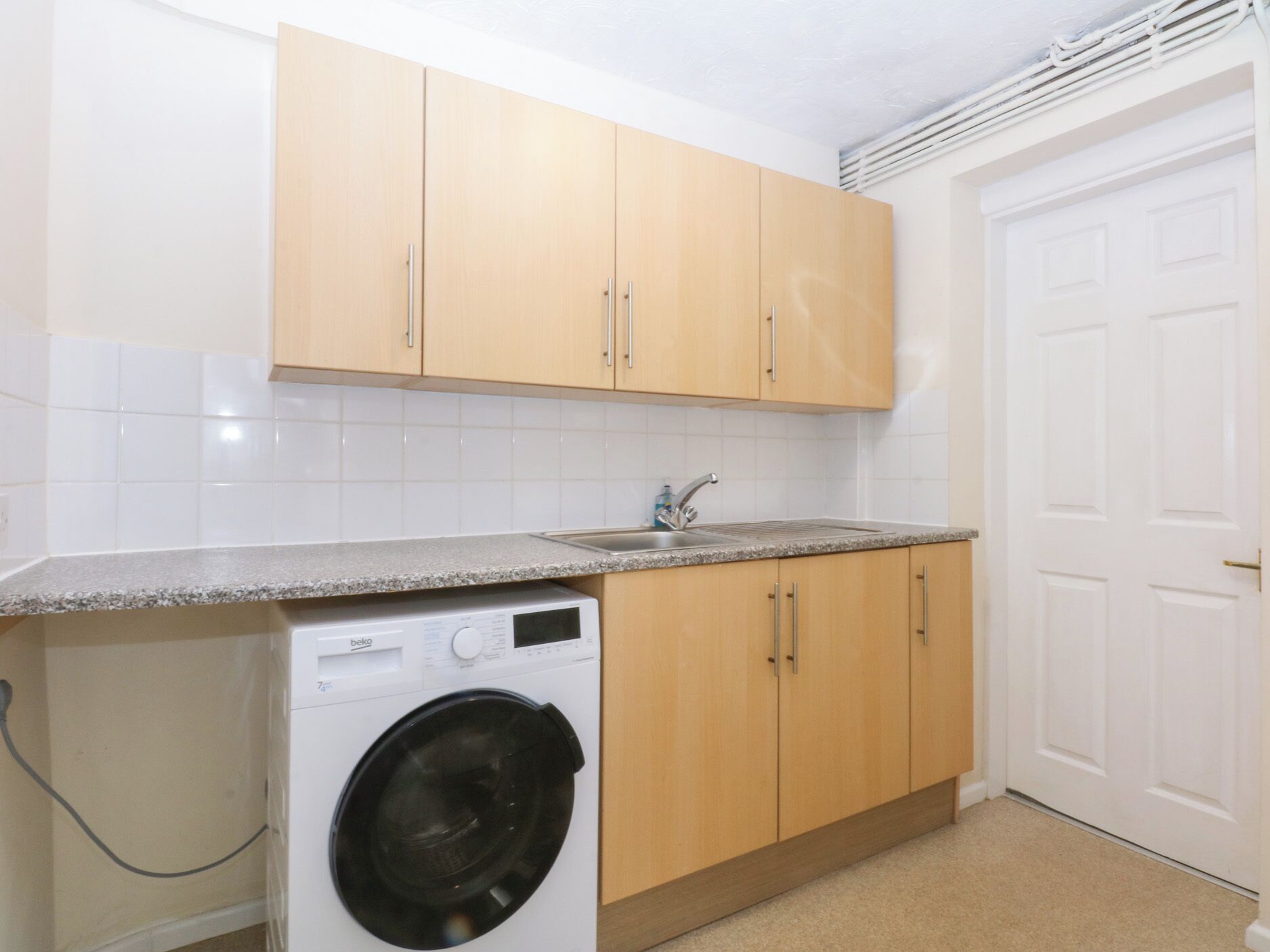 A compact kitchen with wooden cabinets, a built-in washing machine, and a white door.
