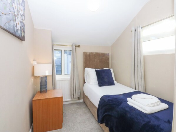 Une chambre à coucher avec un lit, une table de chevet, une lampe et une fenêtre avec des rideaux.
