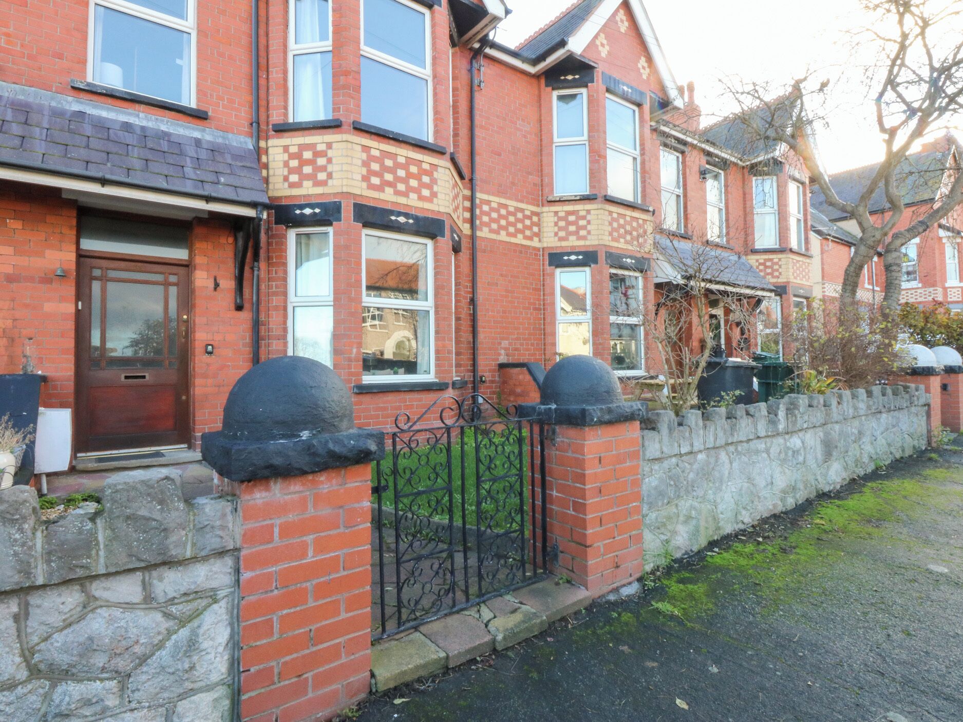 A red brick house with a stone wall and metal gate, featuring a bay window and a front door.
