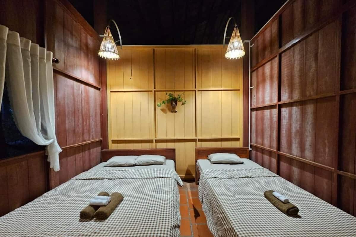 Ein Zimmer mit zwei Betten, Holzwandverkleidung und zwei Pendelleuchten.