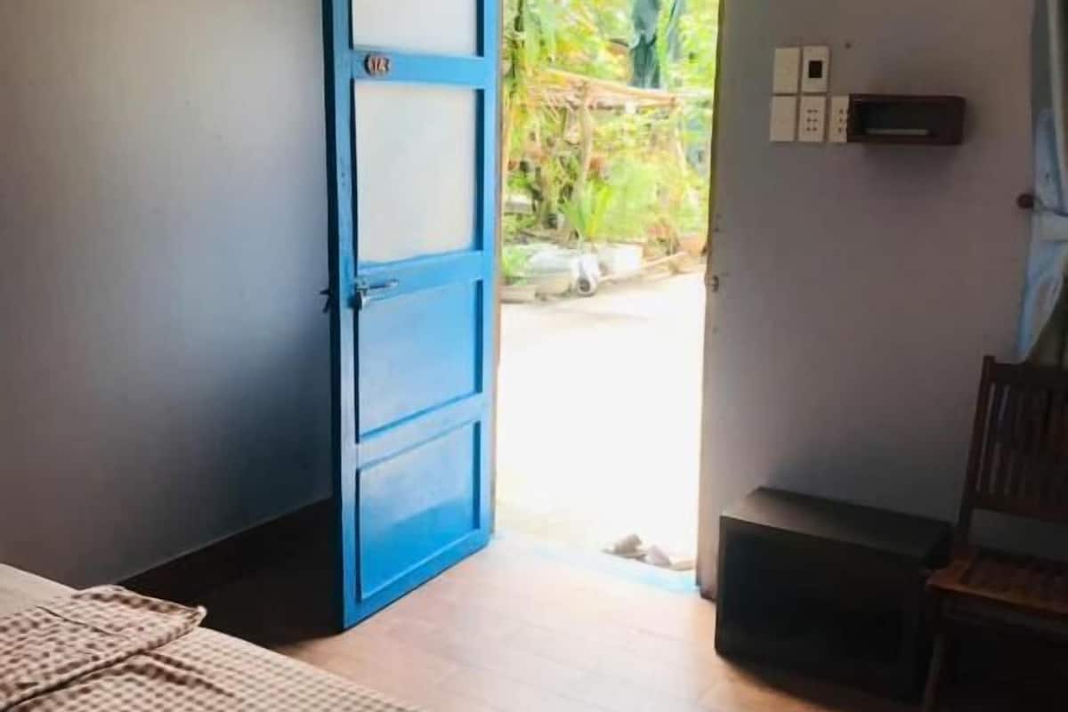 Ein Zimmer mit einem Bett, einer blauen Tür und Blick auf Grün.