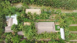 Vue aérienne d’un complexe hôtelier comprenant plusieurs bâtiments, des palmiers et une étendue d’eau.