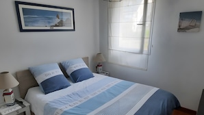 En snyggt bäddad säng med ett randigt överkast, två kuddar, ett sängbord med en lampa och en inramad tavla på väggen.